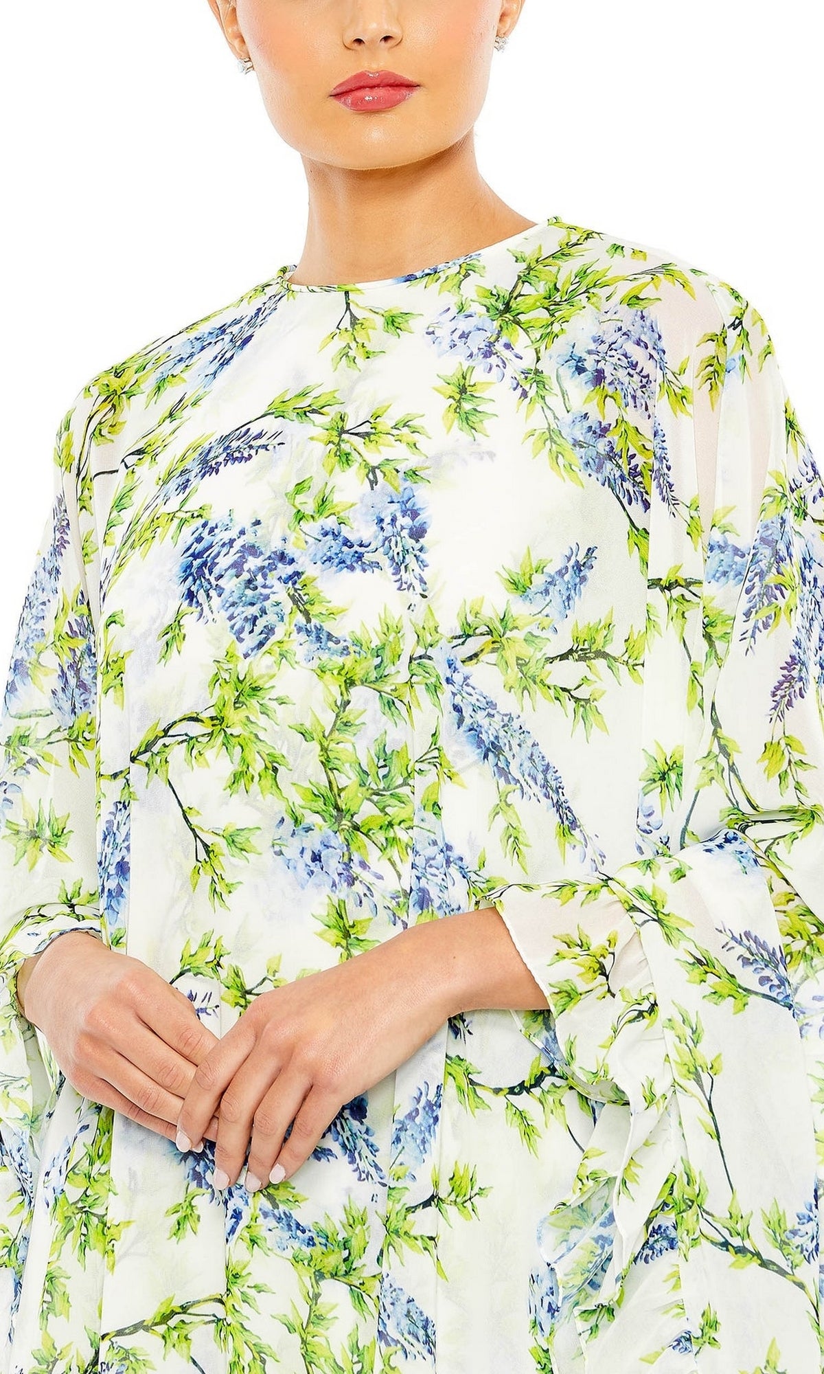 Wearing the Cape Short Party Dress 56029 by Mac Duggal, featuring white fabric with blue and green floral prints, a person stands against a plain background, showing only their lower face and upper body.